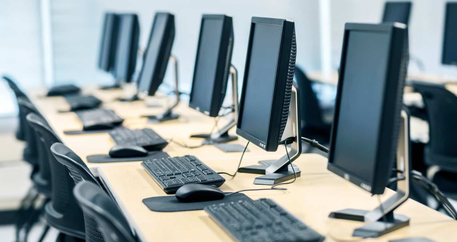 modular ICT suite. Rows of desktop computers with monitors, keyboards, and mice, are placed on long tables in a brightly lit, modern classroom or office setting.